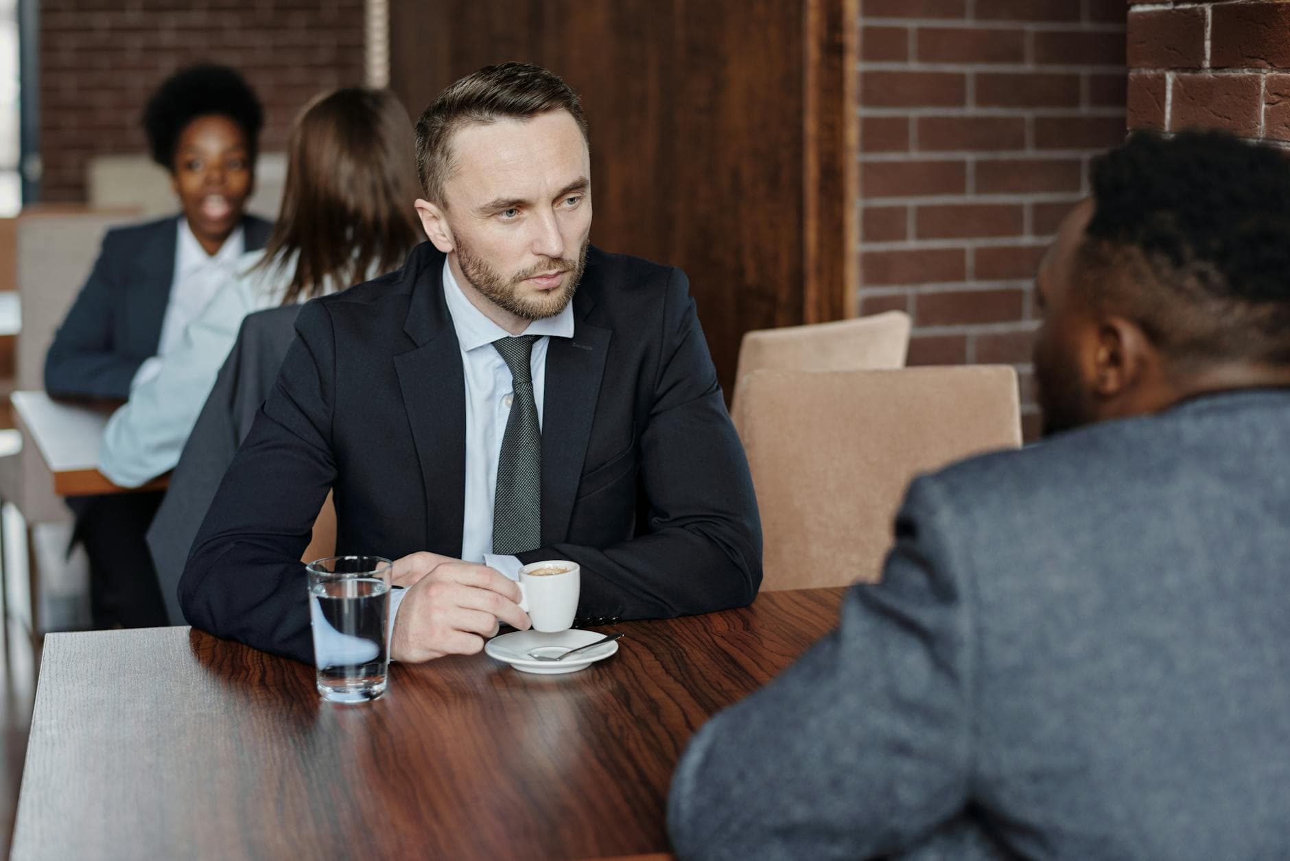 Coach meeting one-on-one with a Keller Williams agent over coffee — bi-weekly accountability conversation