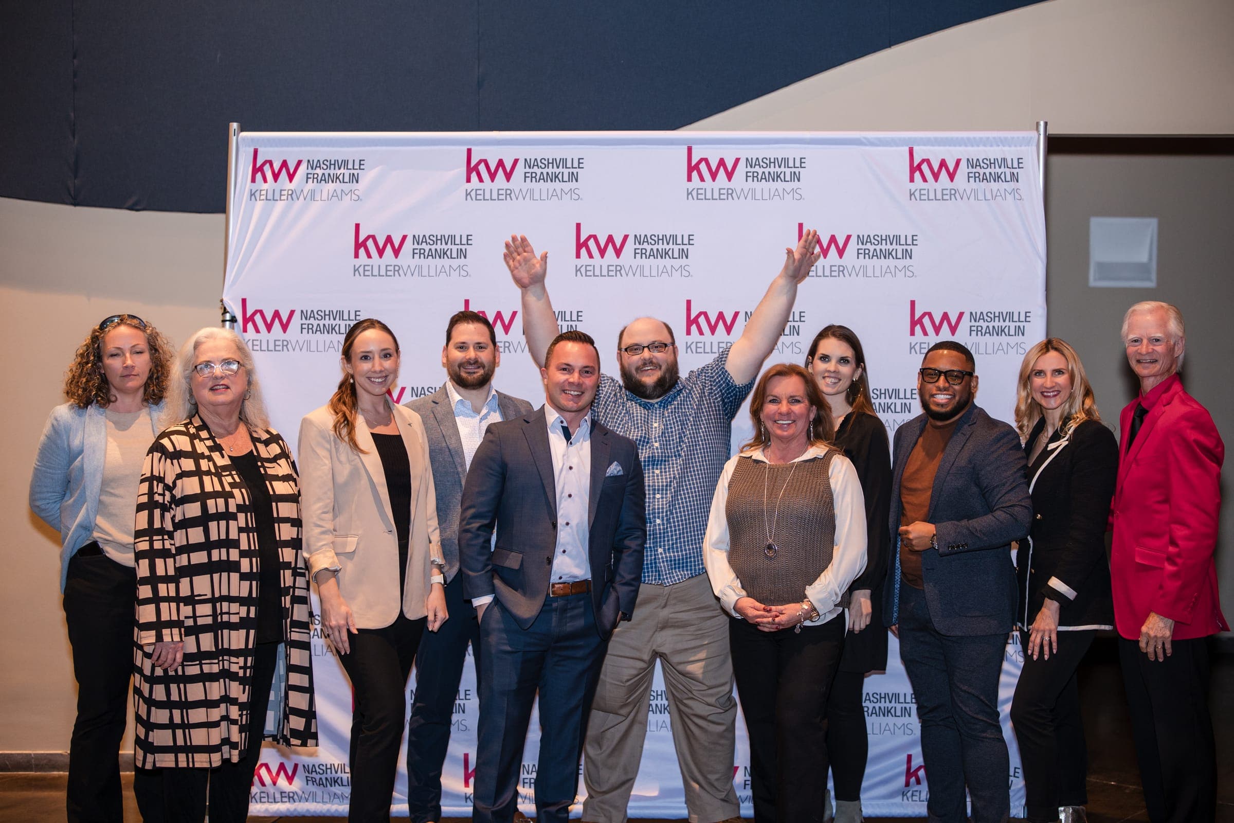 A dozen agents cheering at the Franklin awards celebration, arms raised in front of the KW backdrop