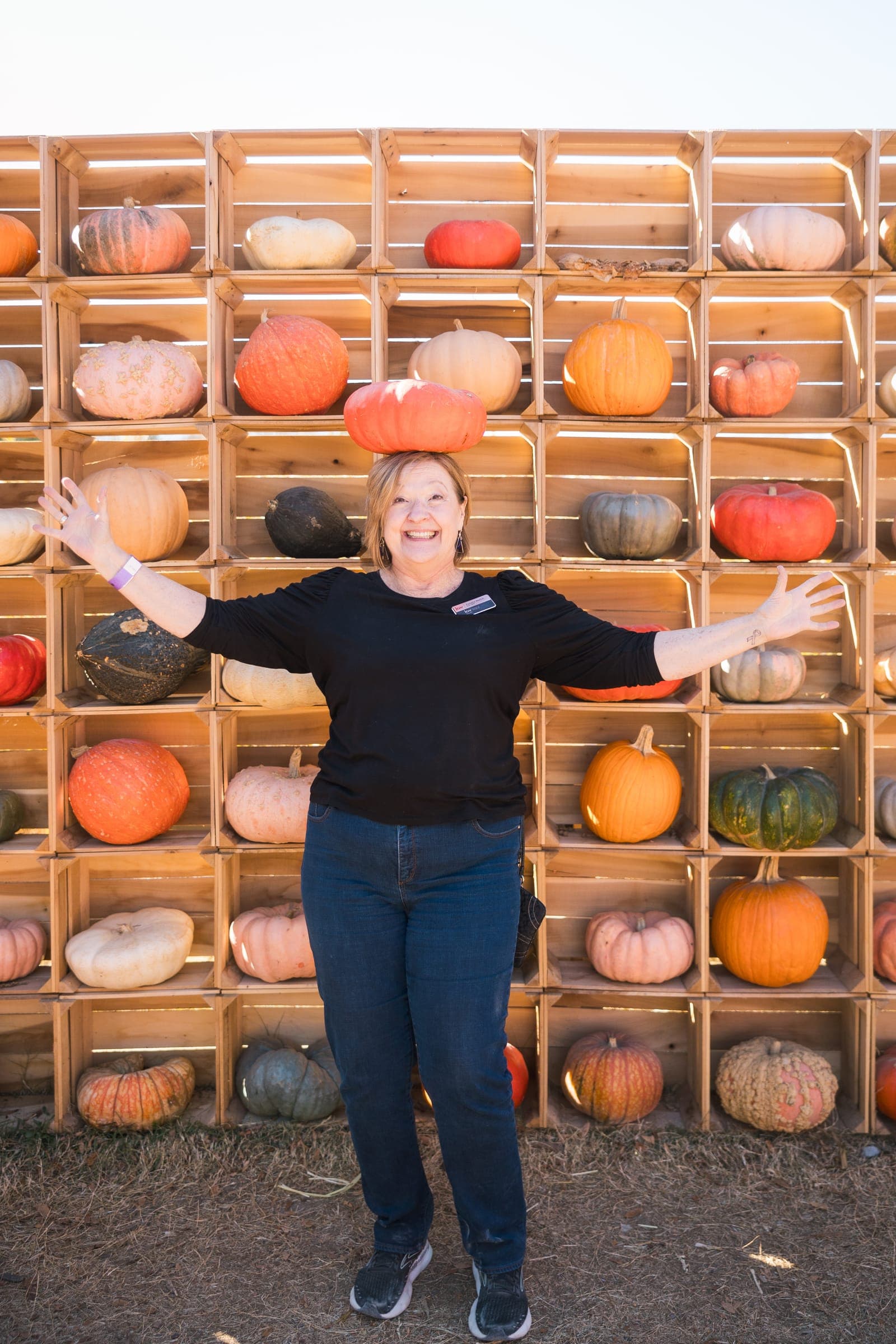 An agent balancing a pumpkin on her head, arms wide, at a Middle Tennessee fall festival crate wall