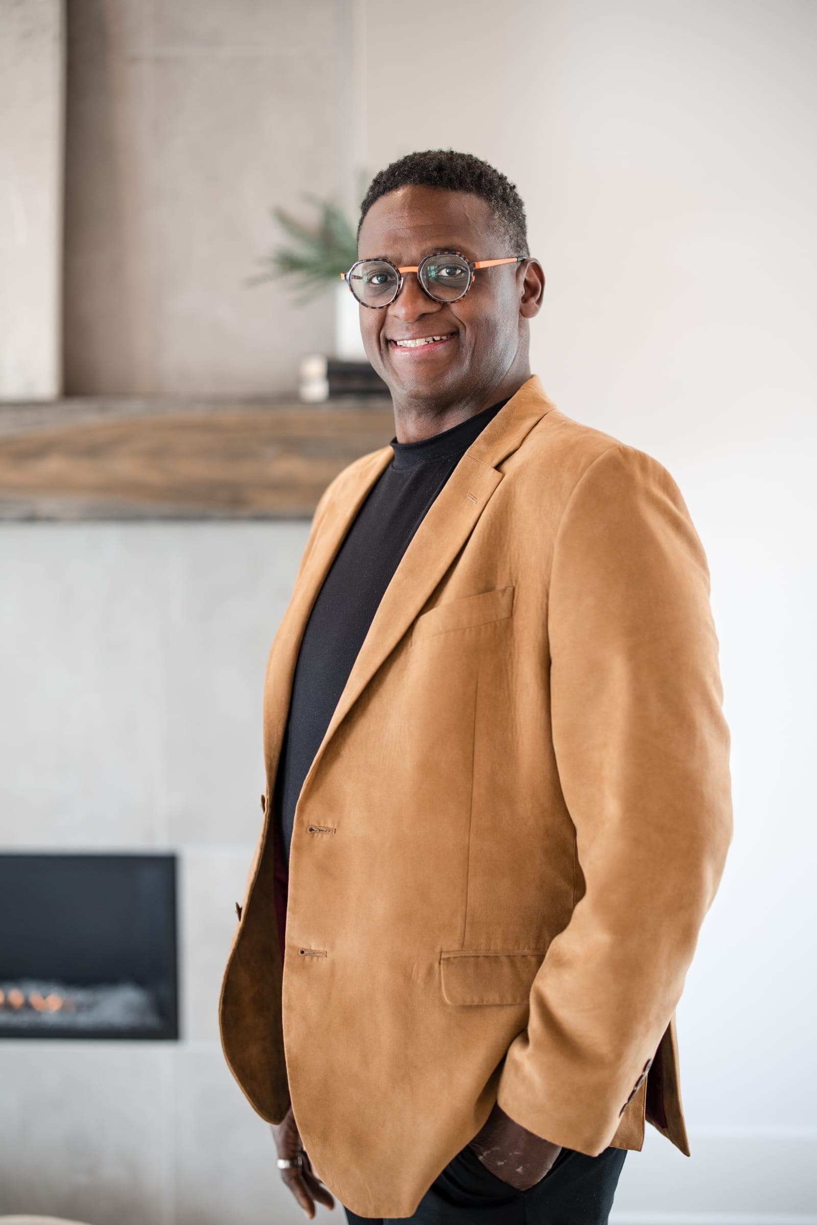 An agent in a camel blazer and round glasses smiling in a staged Middle Tennessee living room