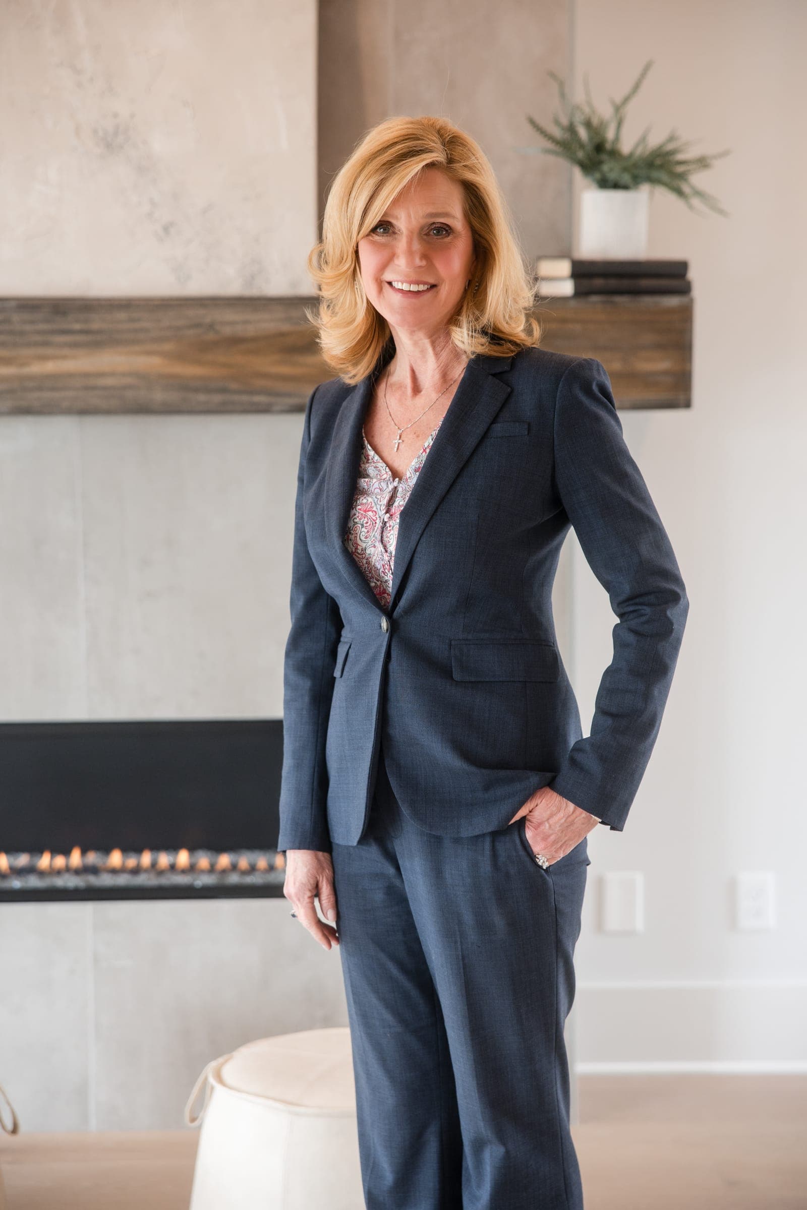 An agent in a navy suit smiling beside a modern fireplace in a light-filled Middle Tennessee home