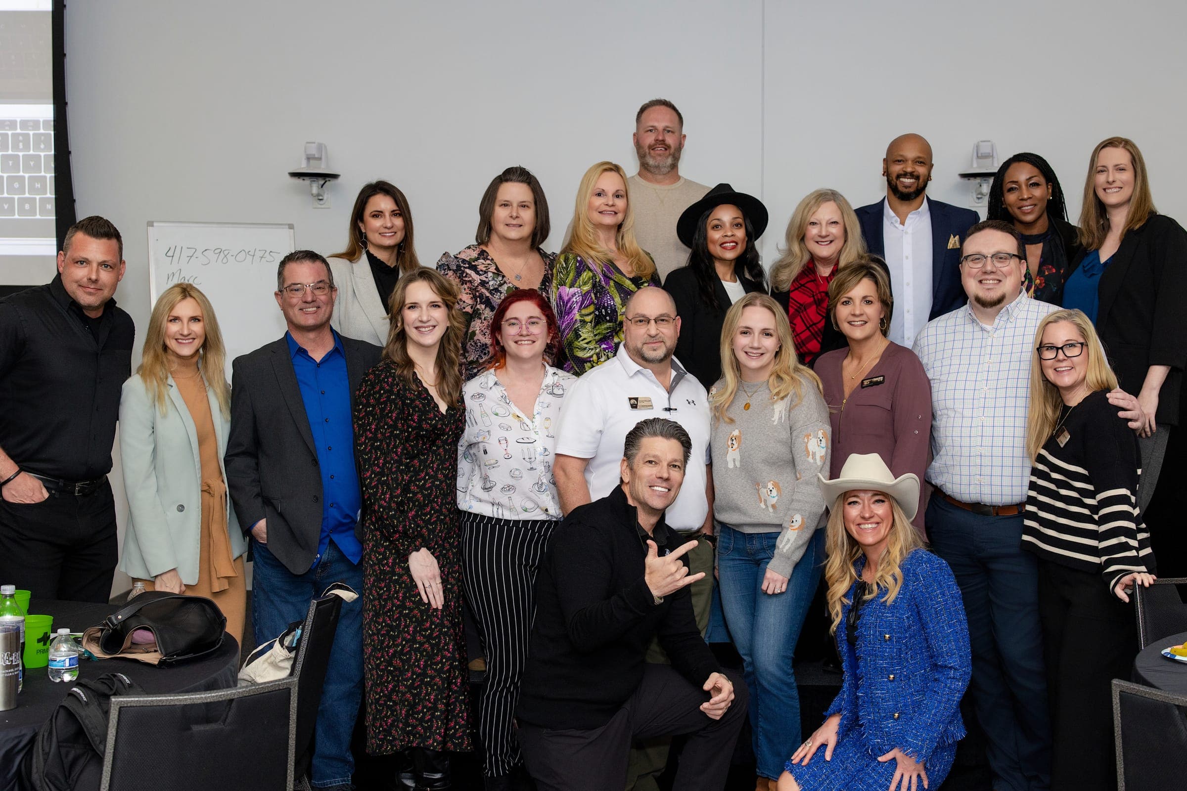 A packed room of Middle Tennessee agents grinning together after a coaching session, arms around shoulders